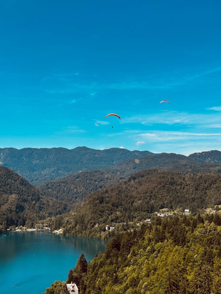 Blick von der Bleder Burg über den türkisen See, am Himmel ein Gleitschirm.