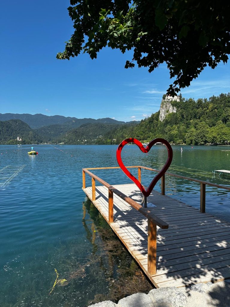 Ein rotes Herz aus Metall auf einem Holzsteg am Bleder See, dahinter die Insel.
