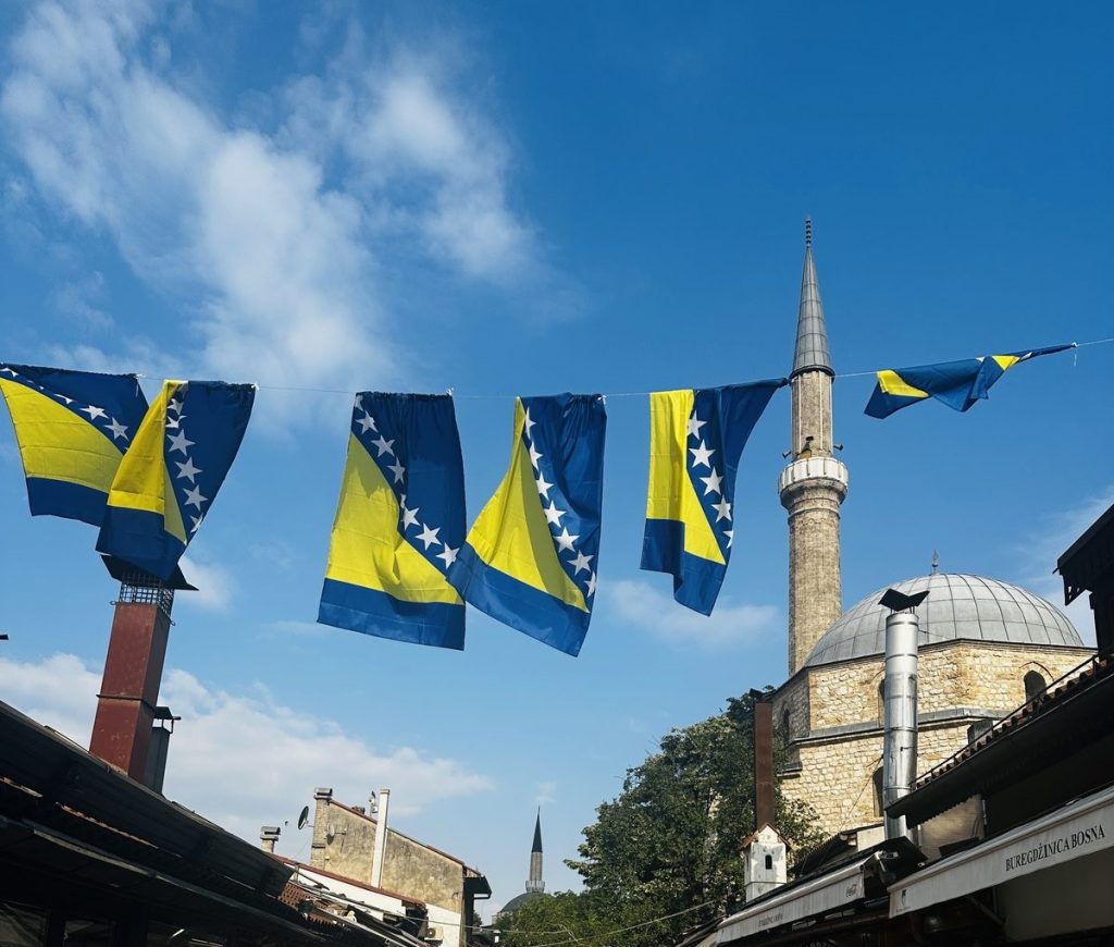 Bosnische Flaggen spannen sich über eine Gasse der Sarajevoer Baščaršija, im Hintergrund ein Minarett