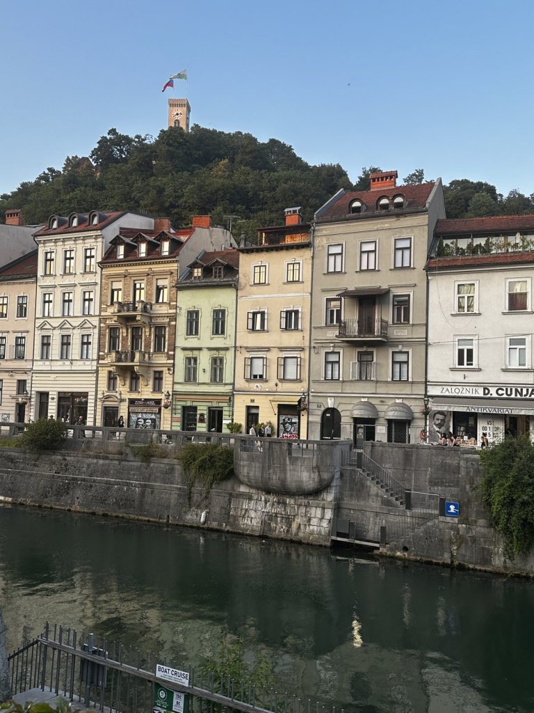 Bunte Häuserzeile am Fluss Ljubljanica, dahinter die Burg auf dem Hügel.