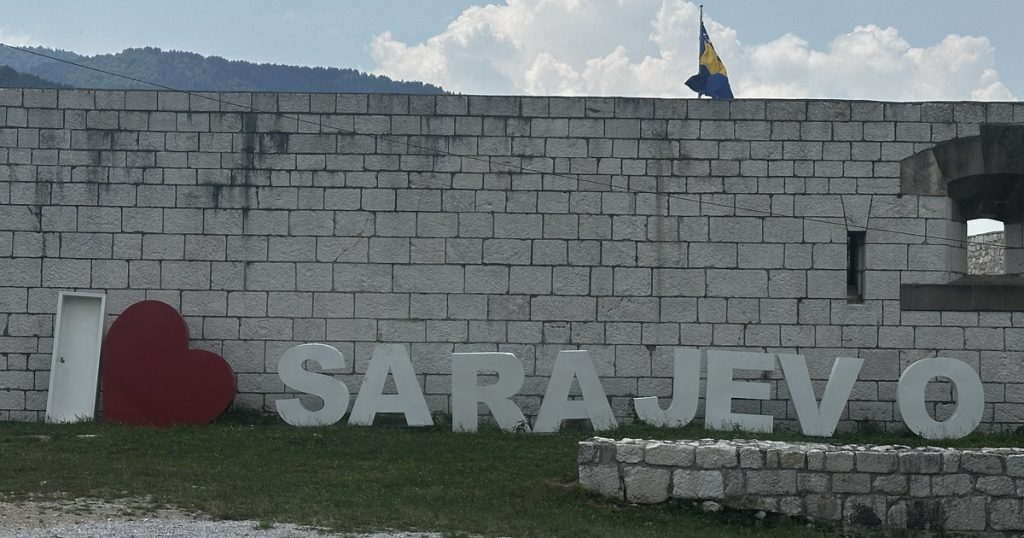 Der Schriftzug „I ♥ Sarajevo" an der Mauer der Weißen Festung, dahinter die bosnische Fahne und die Berge über der Stadt.