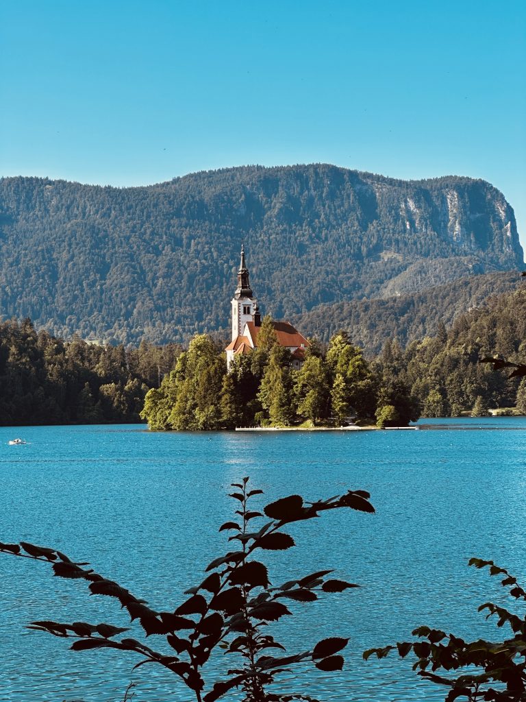 Der Bleder See mit türkisem Wasser und der Inselkirche vor bewaldeten Bergen.