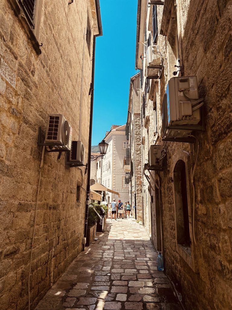 Enge, sonnendurchflutete Altstadtgasse in Kotor mit Klimageräten an den Steinwänden.